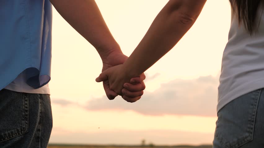 Couple man and woman taking hands to each other at sunset sky summer meadow romantic date closeup. Enamored male and female holding arms together with love tenderness best feelings outdoor back view