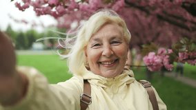 Beautiful happy traveler senior 50s woman taking selfie in park with blossoming sakura trees. Travel spring season of Japanese flower concept, - Powered by Shutterstock - Get 15% off with code: PIKWIZARD15