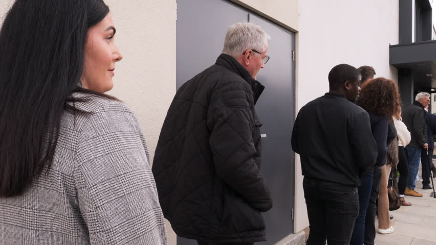 4K: People stand in line outside stood waiting.  People queuing up looking impatient. Back view. Stock Video Clip Footage