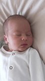 Cute baby is slowly falling asleep. He blinks his eyes and smiles a little. Sleepy sweet child look from above. Vertical video