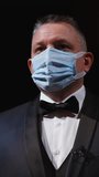 Man in elegant suit and medical mask. Portrait of an actor in protective facial mask standing on stage of a theater. Man putting off mask from face. Coronavirus pandemic. Vertical video