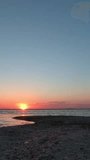 A man with a backpack walks along the sea towards the sunrise. Vertical Video