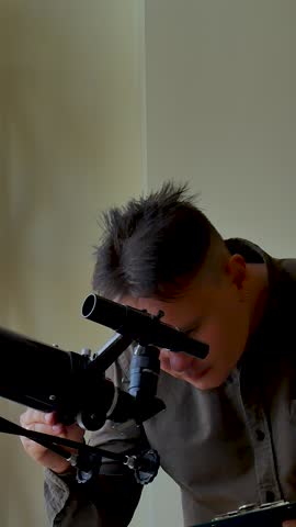 Man looks skyward through astronomical telescope stand near window. Male amateur explore astronomy and analyze star or planet