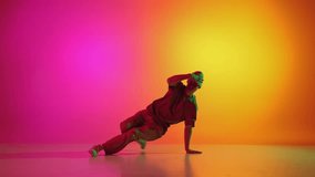 Young, stylish dressed man dancing in vibrant neon light against gradient pink-yellow background. Breakdance. Concept of hobby, sport, creativity, fashion and style, motion, action. Ad