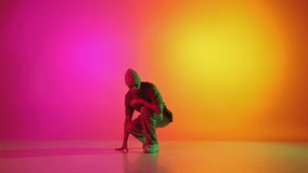 Talented solo artist, male break-dancer performing hip-hop in neon light against gradient pink-yellow background. Concept of art, hobby, sport, creativity, fashion and style, action. Ad
