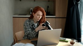 Portrait of smiling young woman photographer holding digital camera looking at screen choosing photos for editing while sitting in front of laptop computer at home workplace. Shooting in slow motion. - Powered by Shutterstock - Get 15% off with code: PIKWIZARD15