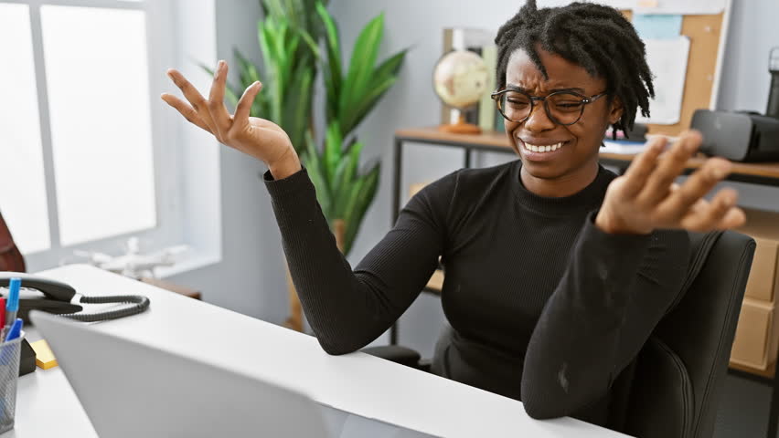 Clueless young black woman with dreadlocks, shrugging her shoulders at the office, puzzled face expression while working on laptop, embodying the doubt concept. Royalty-Free Stock Footage #3481906069