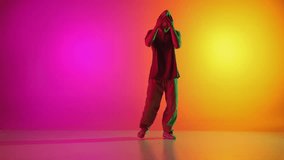Young athletic man dressed streetstyle clothes dancing on hands in neon light against gradient pink-yellow background. Concept of art, hobby, sport, creativity, fashion and style, action. Ad