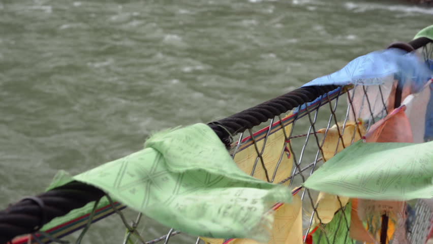 Waving Colorful Prayer Flags On Tibetan Bridge Over River Near Sichuan Village In China. Closeup Shot