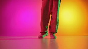 Cool attitude young, man performing breakdance steps in motion in neon light against gradient pink-yellow background. Concept of art, hobby, sport, creativity, fashion and style, action. Ad
