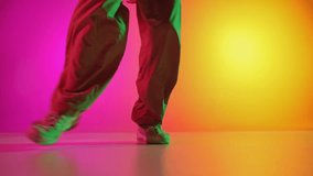 Male dancer in sports attire performing breakdance in motion in neon light against gradient pink-yellow background. Concept of art, hobby, sport, creativity, fashion and style, action. Ad