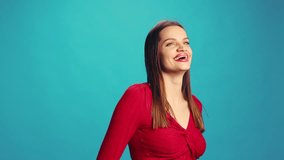Happy young beautiful woman in red blouse posing with happiness, smiling, laughing against blue studio background. Concept of human emotions, facial expression, lifestyle