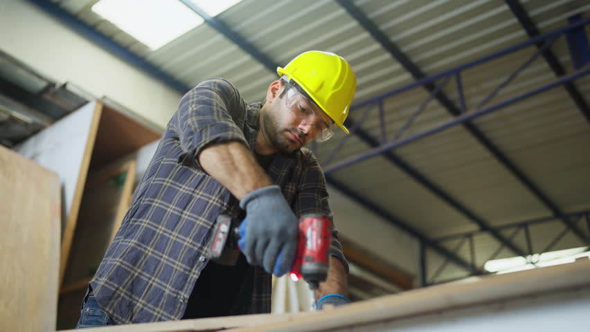 Close up and lower view carpenter or woodworker or charpentier man use drill to work with wood product in workplace.