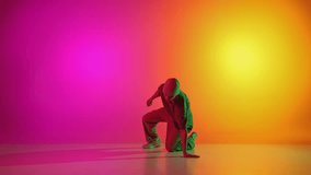 Self-expression through moves. Contemporary dancer dancing hip-hop in neon light against gradient pink-yellow background. Concept of art, hobby, sport, creativity, fashion and style, action. Ad