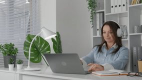 A cozy and comfortable workplace at desk where woman is working and studying with laptop and her notebook. A woman in bright office is smiling because she has successfully completed her work, prepared