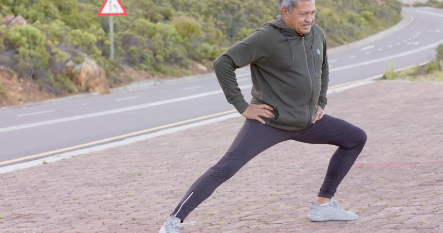 Happy senior biracial man stretching at road in mountains. Hiking, retirement and healthy lifestyle concept.