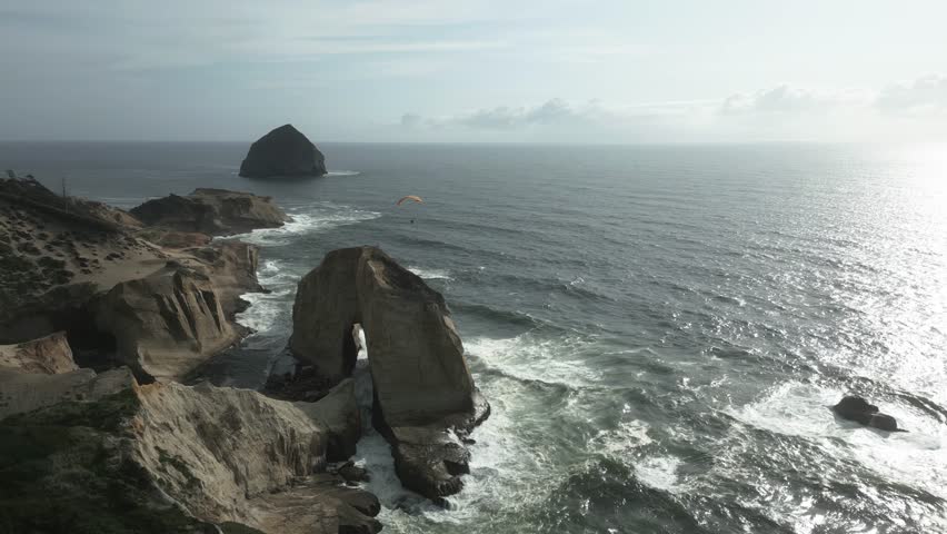 The coastal scenery of Cape Kiwanda along the Oregon coast, USA, is adorned with majesty. A paraglider adds to the allure as it gracefully soars over coastline, exploration amidst nature