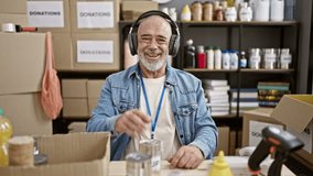 A smiling, senior man with headphones volunteers at an indoor charity event, organizing canned food and other donated items in a storeroom. - Powered by Shutterstock - Get 15% off with code: PIKWIZARD15