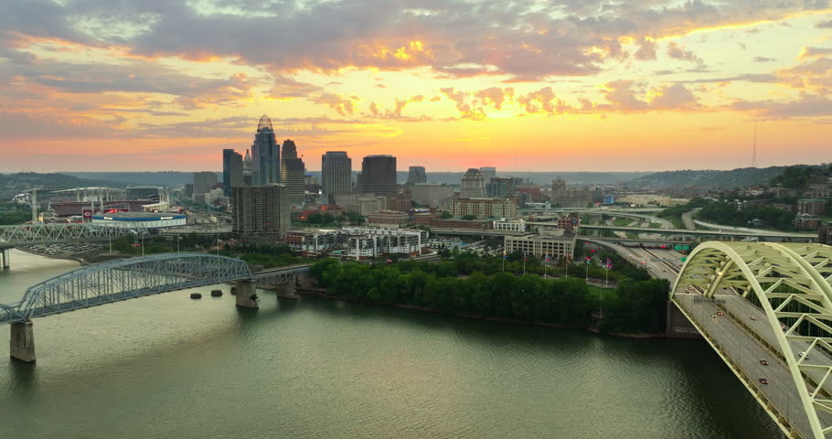 Highway traffic with driving cars on bridge in downtown district of Cincinnati city in Ohio, USA. American city skyline with brightly illuminated high commercial buildings at sunset.