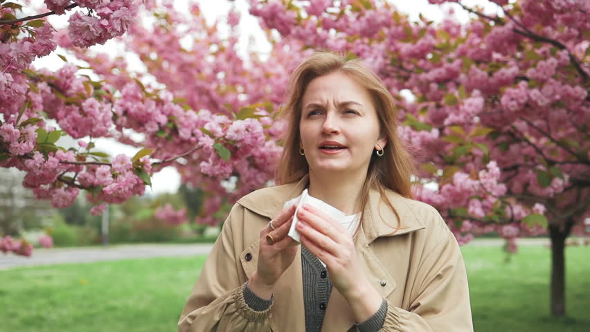Health issues. Pretty young blonde woman having alergy symptoms from blooming sakura tree pollen in spring. Female with pollen allergies of sneezing outdoors Royalty-Free Stock Footage #3482166349