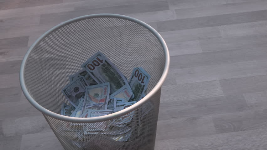 Throwing wad of dollar bills on the paper trash can, wooden floor background.