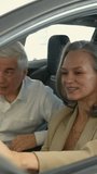 An elderly couple chooses a new car at a car dealership. Mature woman driving. Vertical video. 