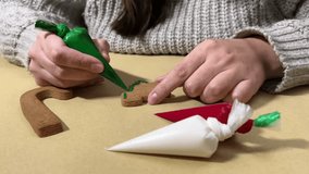 4K video. Woman paints gingerbread tree in shape of Christmas tree on craft table surface. Female hands hold plastic bag with green paint. Preparation for winter holiday concept. Happy New Year 2025