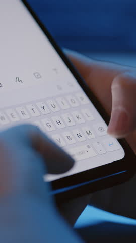Vertical close up of female hands holding smartphone typing message with thumbs indoor at night