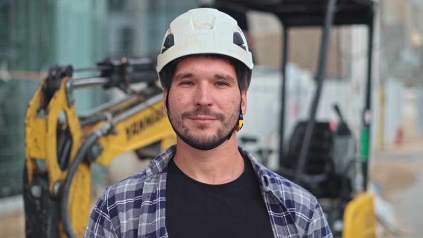 Confident construction site worker portrait. Smile constructor man look camera. Builder engineer wear white helmet. Excavator driver plaid shirt. Guy build new house city street. Erector person job.