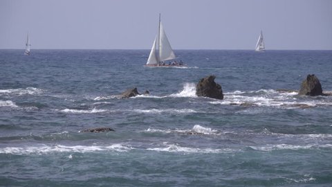 Scene of waves crashing against sharp rocks near a sailboat