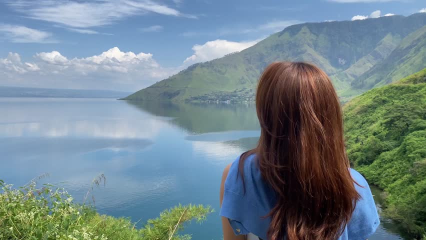 Indonesian woman is looking at the natural beauty of Lake Toba. Indonesian women vacation on a beautiful lake in Dairi Regency, North Sumatra