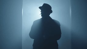  Mysterious silhouette of a man dressed in long coat with hat walking to a dark room through a door. High quality 4k footage - Powered by Shutterstock - Get 15% off with code: PIKWIZARD15