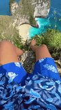 POV of a man sitting on a cliff with a beautiful ocean view at Kelingking Beach, Nusa Penida, Bali, Indonesia. Vertical video summer vacation concept