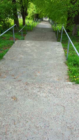 First-person view walking of a downstairs with handrails in green summer park. Vertical, slow motion footage.
