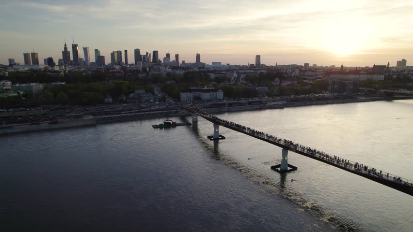 People Walking Through The Agrafka Bridge Over Vistula With City Views At Dusk In Warsaw, Poland. - aerial shot