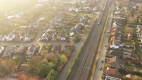 Aerial view of a train running on a track next to residential suburban buildings. Drone video