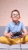 vertical video Portrait of male child with gamepad sitting on sofa 