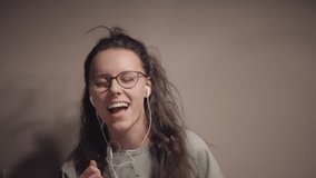 Dancing woman with curly long hair and glasses is smiling while wearing headphones, enjoying the music