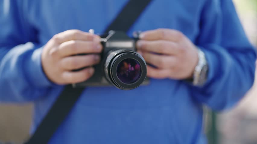 A man is holding a camera with a black lens. He is wearing a blue shirt