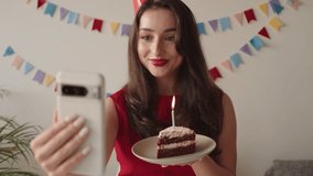 Woman enjoys a solo birthday celebration holding a cake while on a video call with loved ones.