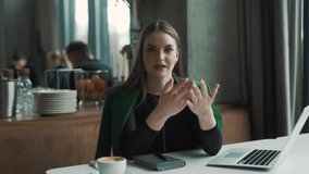 serious, beautiful young woman sitting in a stylish restaurant dressed in business attire talks and argues while looking into the camera - Powered by Shutterstock - Get 15% off with code: PIKWIZARD15