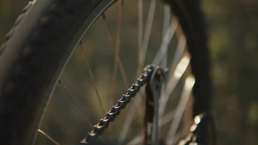 Bicycle chain rotates sprocket and spins wheel in sunlight closeup. Wheel rotates in air and spokes are illuminated by sun. Troubleshooting problems in field during bike rides after falling.