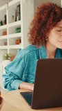 Vertical video, Woman with curly hair wearing denim shirt writing blog on laptop computer