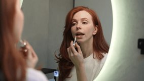 Reflection on mirror of gorgeous young woman applying lipstick get ready preparing for romantic date. Closeup of pretty redhead female model enjoy beauty routine admiring makeup at home, slow motion. - Powered by Shutterstock - Get 15% off with code: PIKWIZARD15