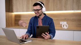 A male student, studying online, uses headphones and a tablet to attend an online education class on the school's video chat platform.
