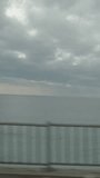 Vertical video. Driving on a bridge along the sea, view of the water and clouds, overcast weather.