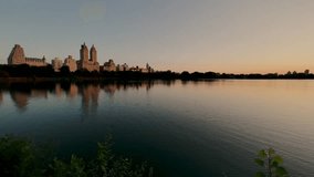 Sunrise from the Jacqueline Kennedy Onassis Reservoir in Central Park, New York. Lake surrounded by New York skyscrapers with reflections on the lake in summer.
