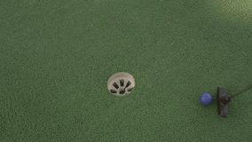 This video shows an overhead view of a mini golf ball being hit into the hole by a golf club.