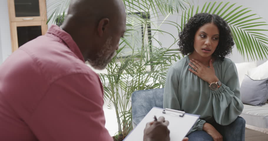 Diverse male therapist holding clipboard and female patient talking in therapy session, slow motion. Mental health, therapy and counselling.