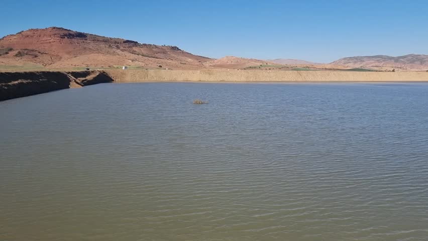 Behold the stunning spectacle from above as a serene lake peacefully lies amidst the vast expanse of the Algerian desert—a true marvel of nature